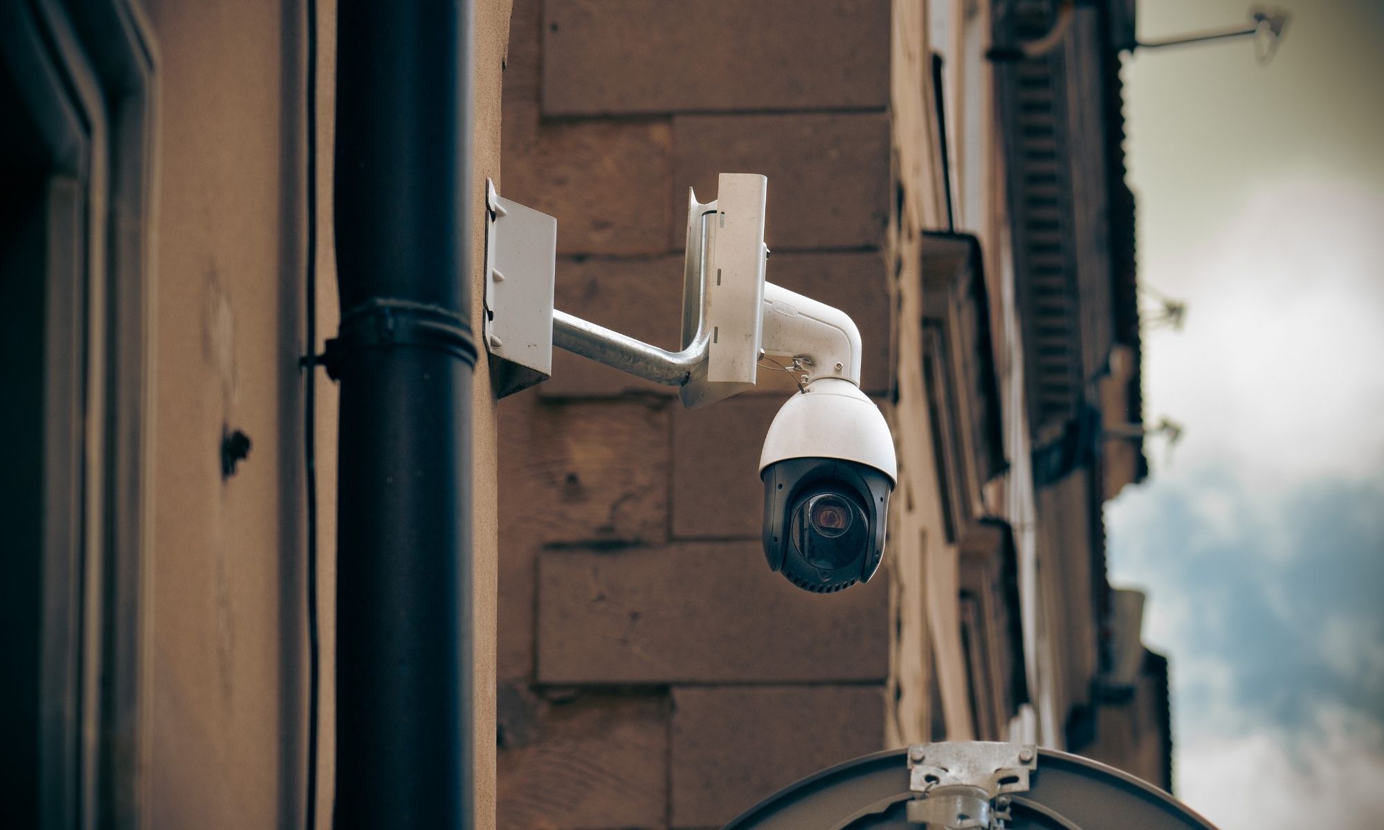 White dome-shaped security camera mounted on an exterior wall, part of the building’s security hardware, overlooking street.