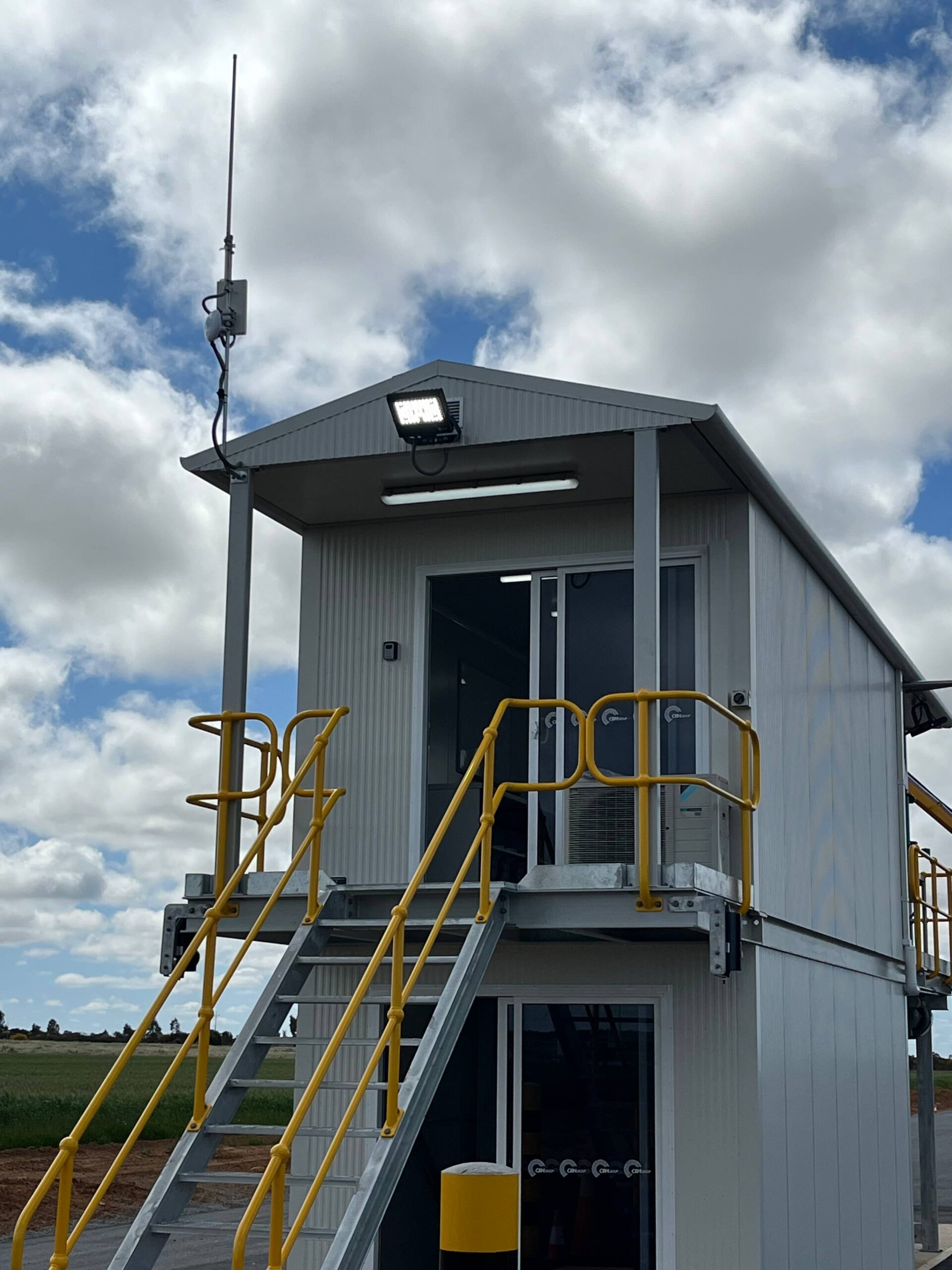 Portable building with yellow railings and metal stairs for commercial security solutions under a cloudy sky.
