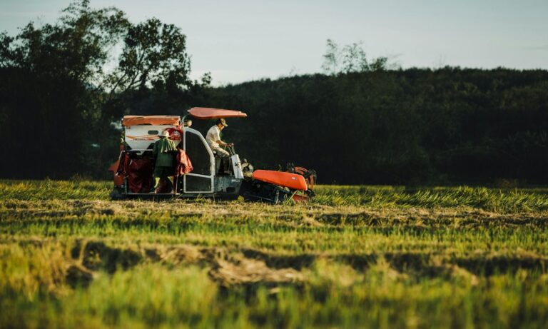 Person using red tractor-like machine in grassy field, stressing fuel & fertiliser storage security on farms.