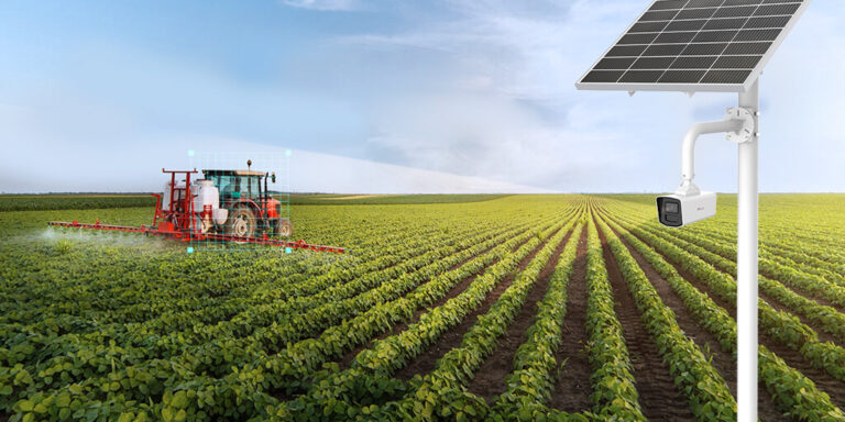 Solar-powered security camera monitors green crop field as tractor sprays plants, under a partly cloudy sky.